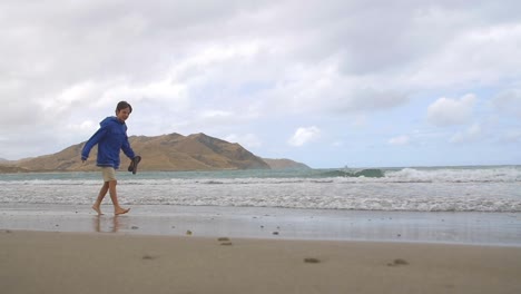 young boy walking along windy beach