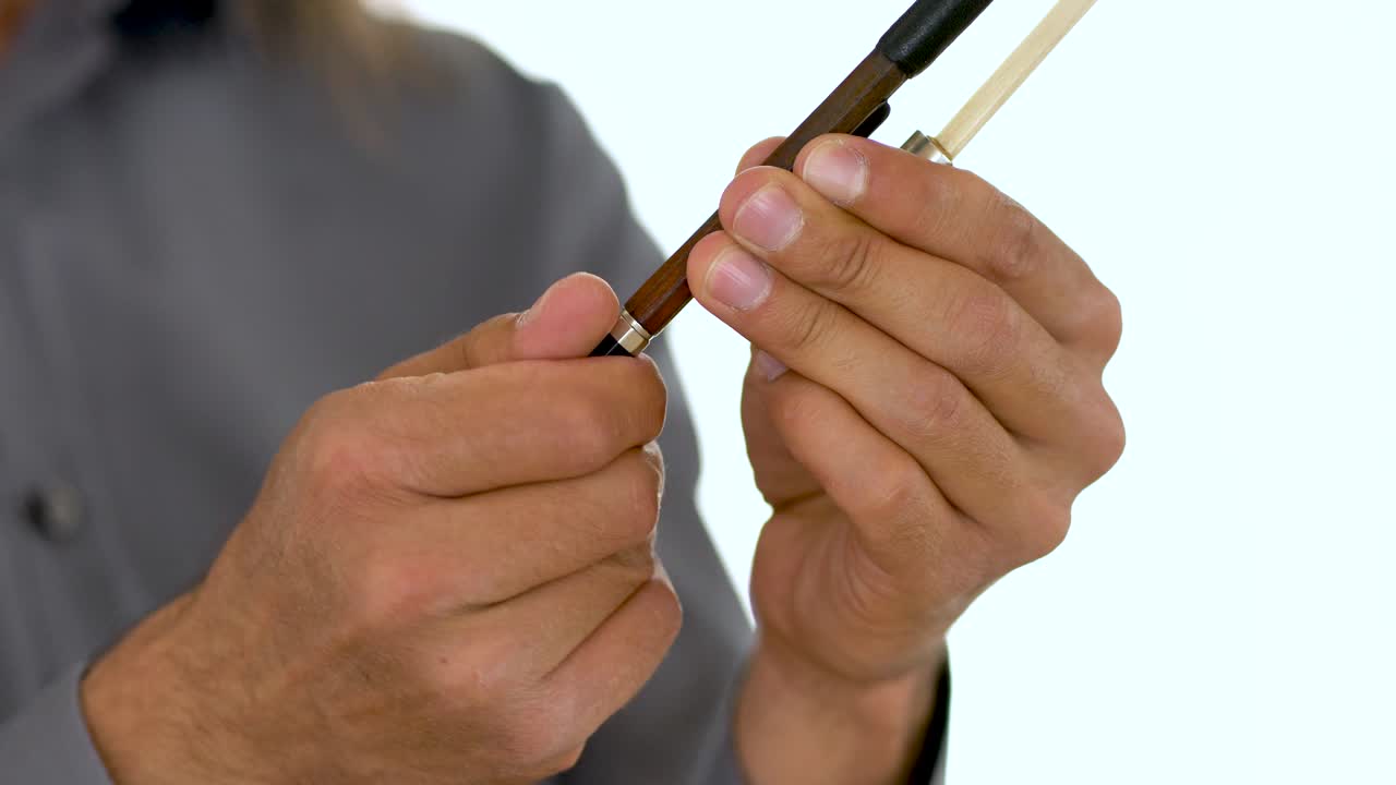 primer plano de manos de músicos étnicos en camisa de manga larga gris apretando arco de violín