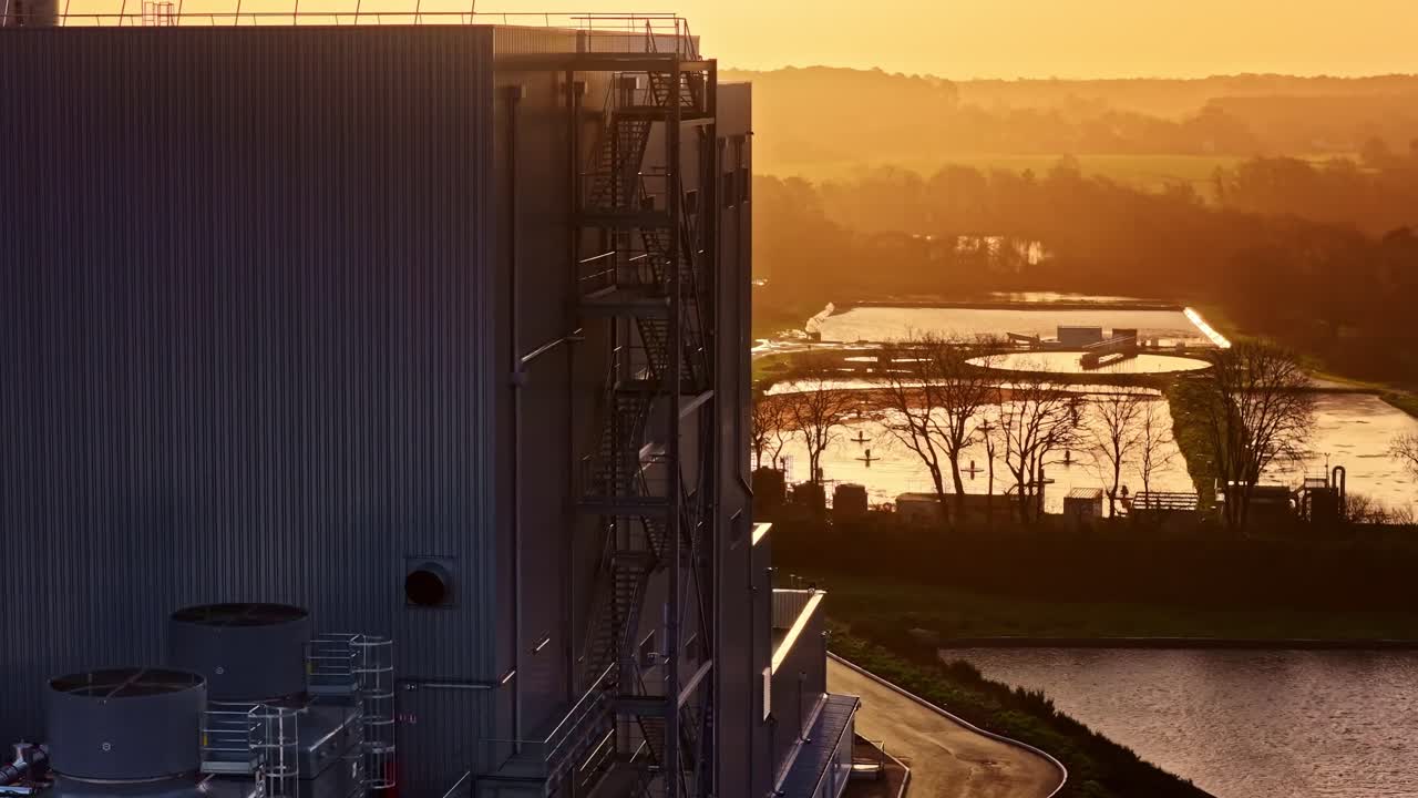 Splendida vista aerea di un moderno impianto di trattamento delle acque reflue con grandi vasche di decantazione e edifici industriali stagliati contro un vibrante cielo arancione al tramonto nel paesaggio rurale della Lettonia