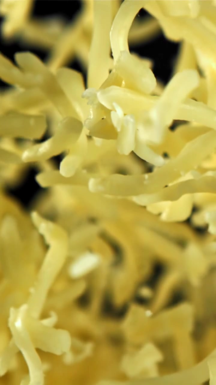 Formaggio giallo grattugiato che cade al rallentatore su sfondo nero