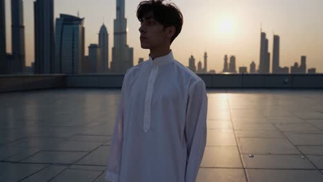 emirati businessman in traditional white kandura stands on a rooftop in dubai. contemplating the cityscape at sunrise. embracing the peace and quiet of the morning before the bustling city awakens