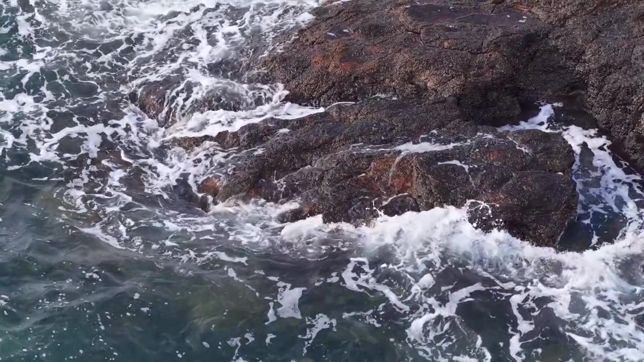Ripresa dall'alto di schiuma marina bianca che turbina intorno a scogli costieri scuri in Australia