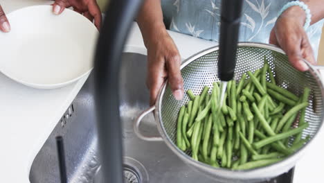 Sección-Media-De-Amigas-Afroamericanas-Mayores-Lavando-Frijoles-En-El-Fregadero-De-La-Cocina,-Cámara-Lenta