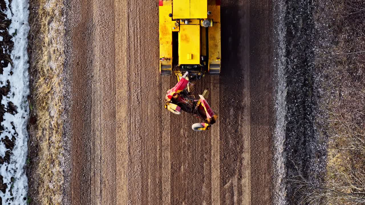 En grader udjævner en grusoverflade til vejvedligeholdelse og reparation, set i fugleperspektiv.