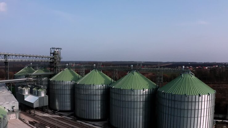 Metal silos on field aerial view. Large containers for storing and processing grains. Silver grain elevators in farmland. Storage tank view from above. Silo with grain.