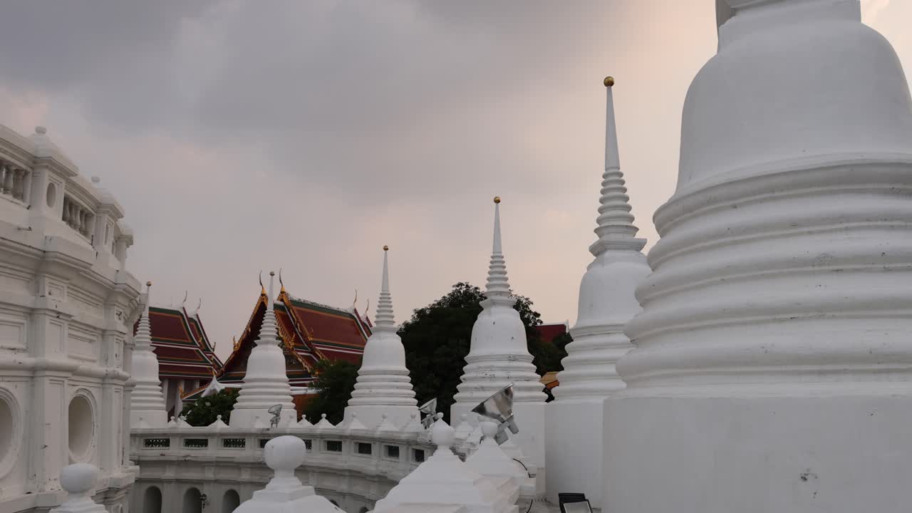 A tranquil scene of Wat Prayurawongsawat in Bangkok, showcasing its iconic white stupas under a cloudy sky