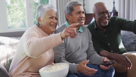 Happy-biracial-senior-couple-and-african-american-friend-watching-tv-with-popcorn