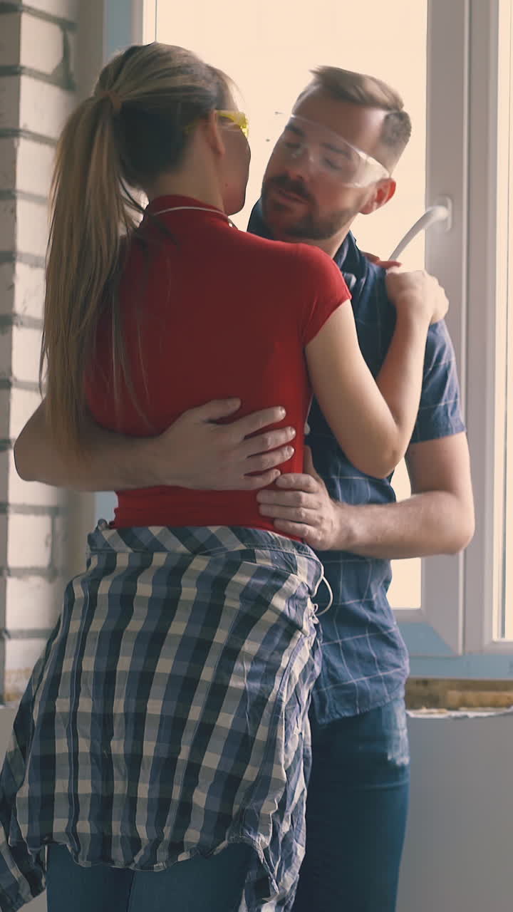bearded man in goggles with pretty young wife apply spray foam insulation on windowsill at construction in light room