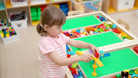 Niña-Creativa-Construyendo-Torre-Con-Ladrillos-Constructores-En-Una-Mesa-Grande-En-La-Sala-De-Juegos---Cámara-Lenta