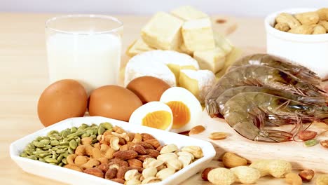 una variedad de alimentos ricos en proteínas, incluidos productos lácteos, nueces y carnes, están artísticamente dispuestos en una superficie de madera