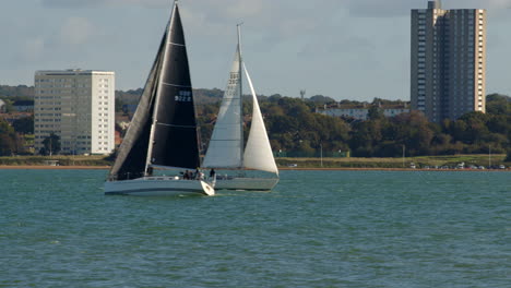 two sailboats cross each other on the solent at southampton with weston in background