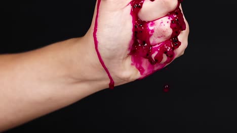 a hand firmly squeezes vibrant red pulp, with juice visibly dripping down against a dark background.