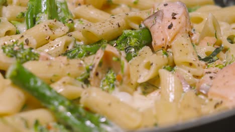 panning across seafood salmon and broccoli penne italian pasta in frying pan with cracked black pepper in a rich creamy sauce. cooking kitchen footage 4k.