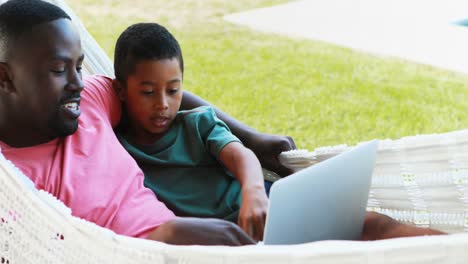 father and son using laptop while relaxing on hammock