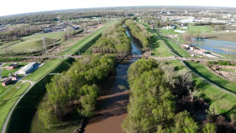 Drone-shot-of-dirty-muddy-creek-river-lots-of-trees-and-greenery-in-a-small-town