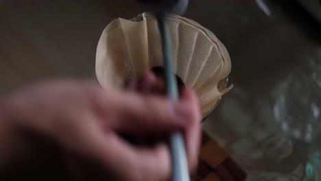 close-up static shot of spoons of ground coffee added to pour over filter paper before brewing