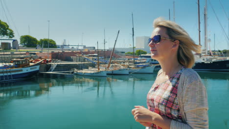 Una-Mujer-Turística-Camina-Por-El-Paseo-Marítimo-De-Barcelona-Con-El-Telón-De-Fondo-Del-Mar-Y-Los-Yates