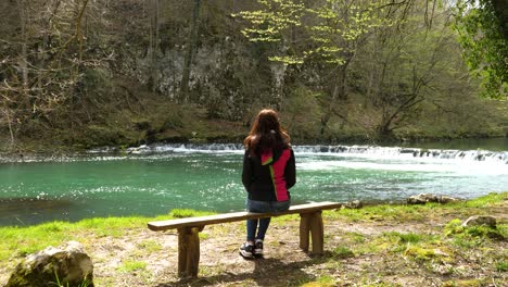 static shot of a woman resting enjoying the views of a small waterfall at the riverside