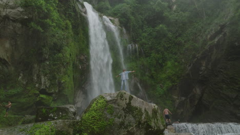 drone captures a male enjoying a majestic waterfall in nepal’s mid-forest during monsoon