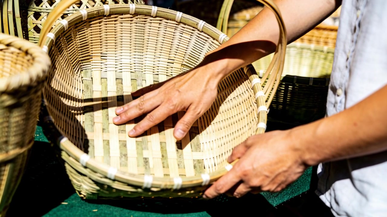 Mani di un adulto con una camicia chiara che ispezionano un cesto di vimini su un panno verde, controllandone la qualità.