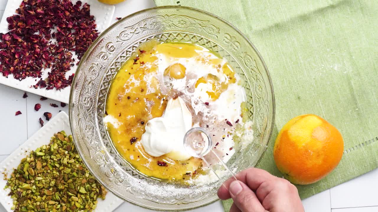 Preparazione di un dolce chiamato Persian Love Cake fatto con petali di rosa e pistacchi. Torta con glassa bianca. Aggiunta dell'estratto di mandorle all'impasto. Bella torta per l'ora del tè o per una celebrazione