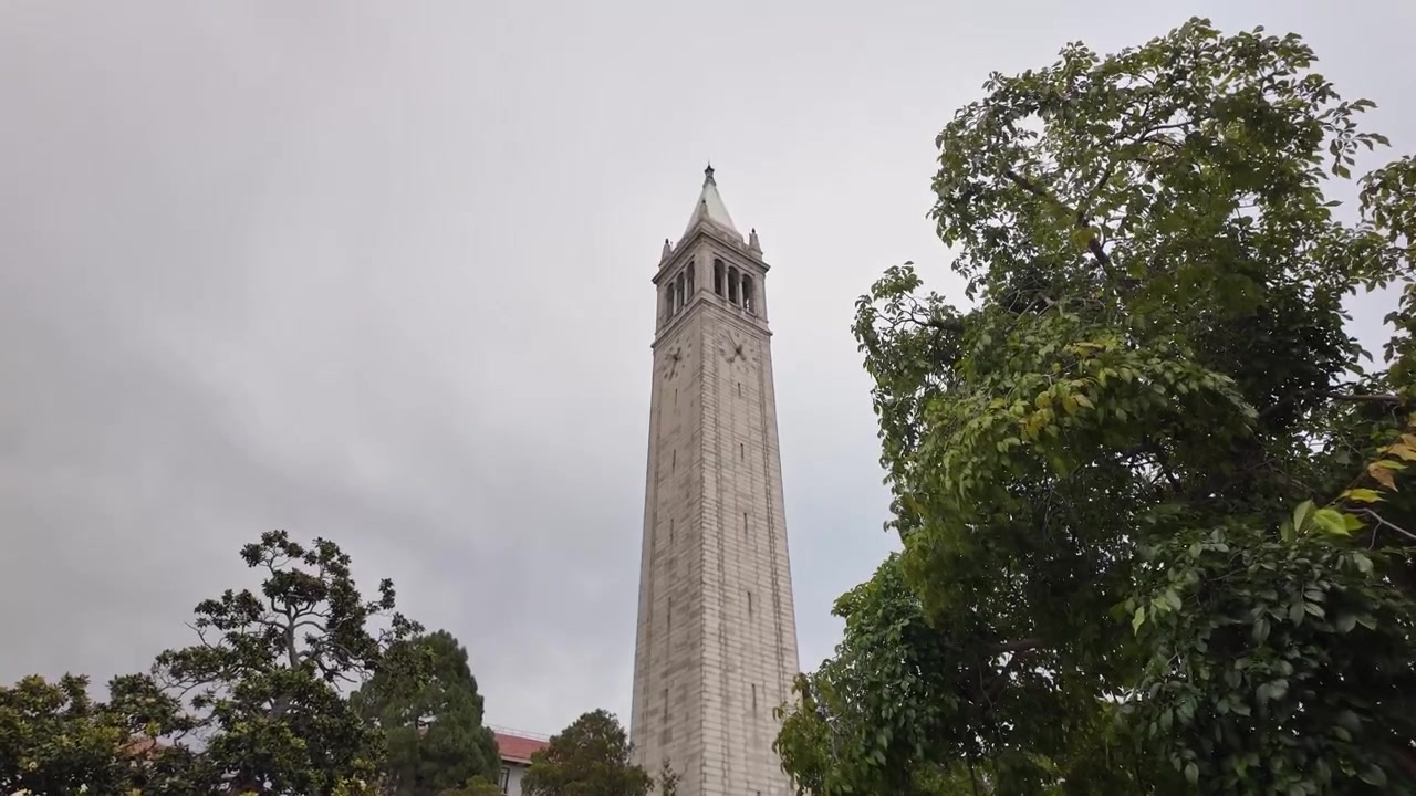 Filmato grandangolare panoramico della Sather Tower all'UC Berkeley, incorniciata da alberi verdi lussureggianti sotto cieli nuvolosi, che mette in mostra l'architettura storica, il campus tranquillo e una luce naturale suggestiva.