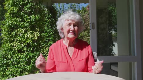 Caucasian-senior-woman-sitting-at-table-in-sunny-garden-talking-and-gesturing