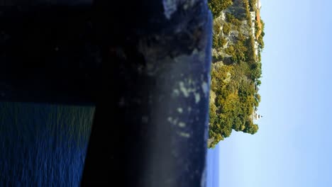 vertical slow motion ascending shot of the beautiful rocks at pura uluwatu temple in bali indonesia overlooking the blue sea while waves crash on the rocks on a sunny day