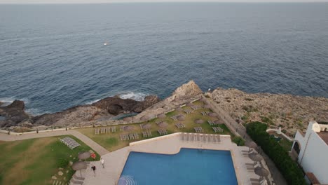 Toma-Aérea-De-La-Espalda-Del-Carro-Sobre-La-Escarpada-Costa-Con-Piscina-Con-Vista-Al-Mar-En-Un-Hotel-De-Lujo-En-Mallorca