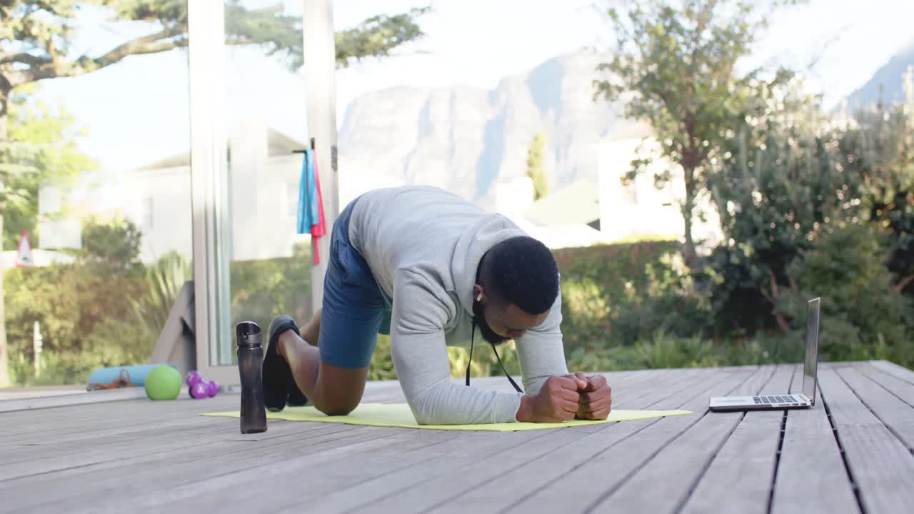concentrado hombre afroamericano entrenamiento de acondicionamiento físico haciendo ejercicio en la cubierta en el jardín soleado, cámara lenta
