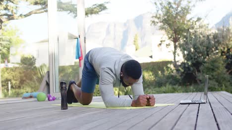 Hombre-Afroamericano-Enfocado-En-Entrenamiento-Físico-Haciendo-Ejercicio-En-Cubierta-En-Un-Jardín-Soleado,-Cámara-Lenta