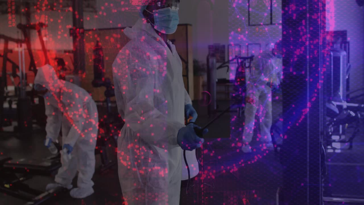 Dopo aver regolato lo spruzzatore, un tecnico pulisce l'attrezzatura da palestra per la sanificazione, mentre particelle animate turbinano.