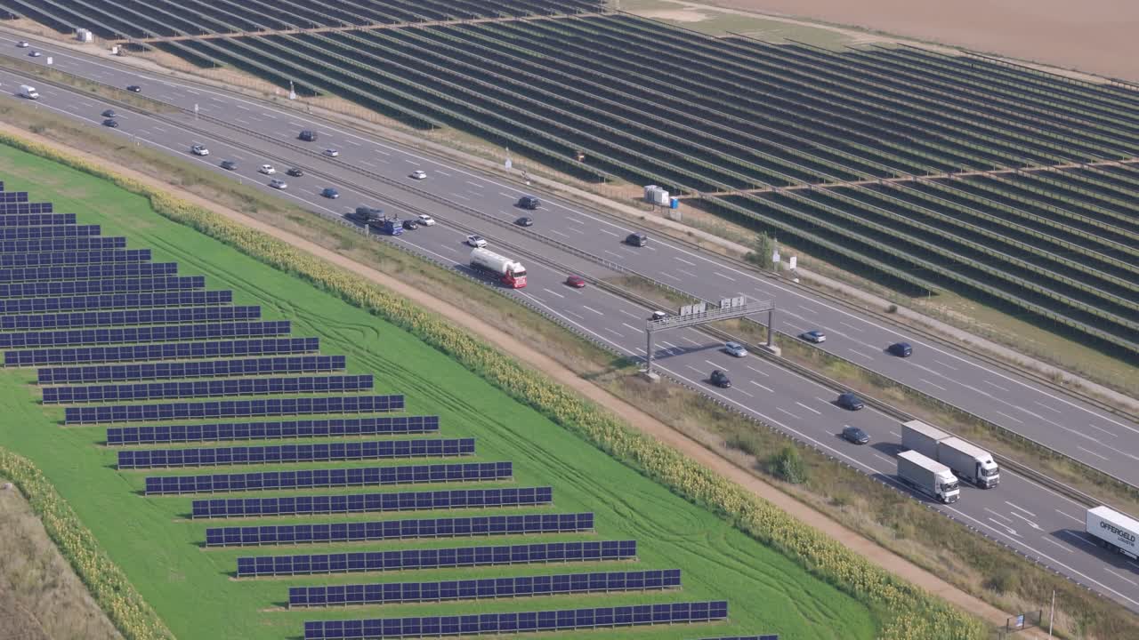 Highway cuts through two large solar parks, one with east-west vertical panels, Germany, high angle drone view