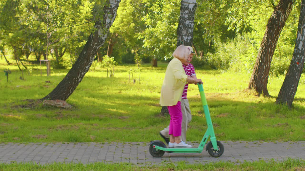 Anziani turisti eleganti, nonna e nonno, che usano uno scooter elettrico mentre guidano nel parco