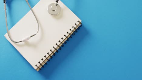 video of stethoscope on notebook, on blue background with copy space