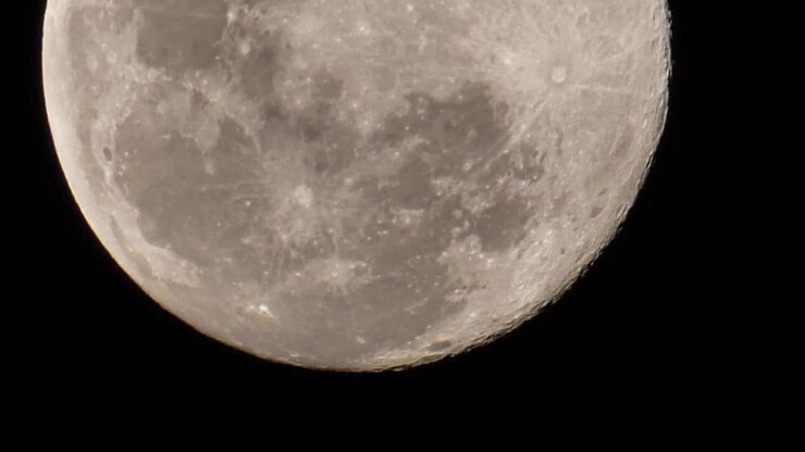Vista de uma lua cheia enquanto se move lentamente um pouco para cima, mostrando as crateras e outras formações geológicas visíveis na superfície lunar.
