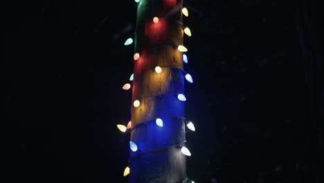 Winter snowfall at night snowing on Christmas lights on city street in street light