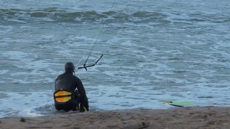 man engaged in kitesurfing, overcast winter day, high waves, baltic sea karosta beach , slow motion, medium shot