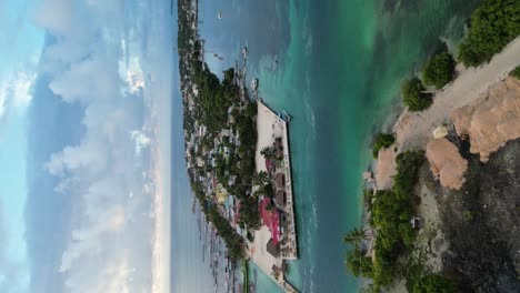 drone portrait view in belize flying over caribbean dark and light blue sea, a white sand caye covered with palm trees and restaurants on a cloudy day