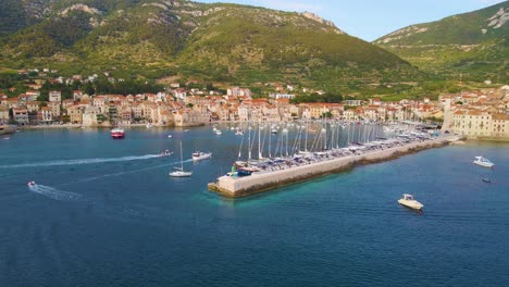 Panorama-De-Un-Pueblo-Costero-Con-Muchas-Casas-Con-Techos-Rojos,-Rodeado-Por-El-Mar-Y-Las-Montañas-Con-Un-Largo-Muelle