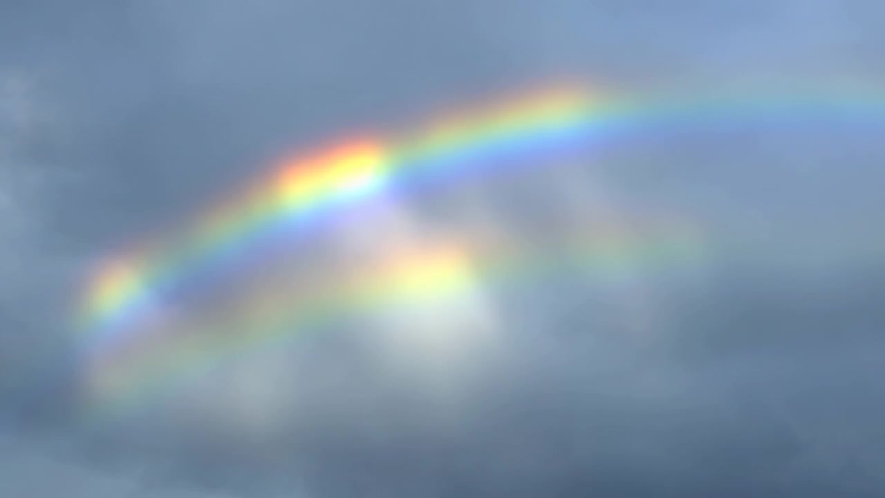 Arco di arcobaleno parziale si estende nel cielo superiore sopra spesse nuvole stratiformi grigio-blu, con il colore più brillante vicino alla cresta, un debole bagliore secondario, tenui tonalità pastello e una tranquilla scena meteorologica atmosferica.