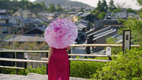 woman in wagasa umbrella walks at the yasaka pagoda viewpoint, looks at the japanese house in kyoto, japan