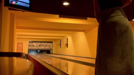 girl playing bowling and missing the pins. we are in a dimly lit bowling space during the night time.
