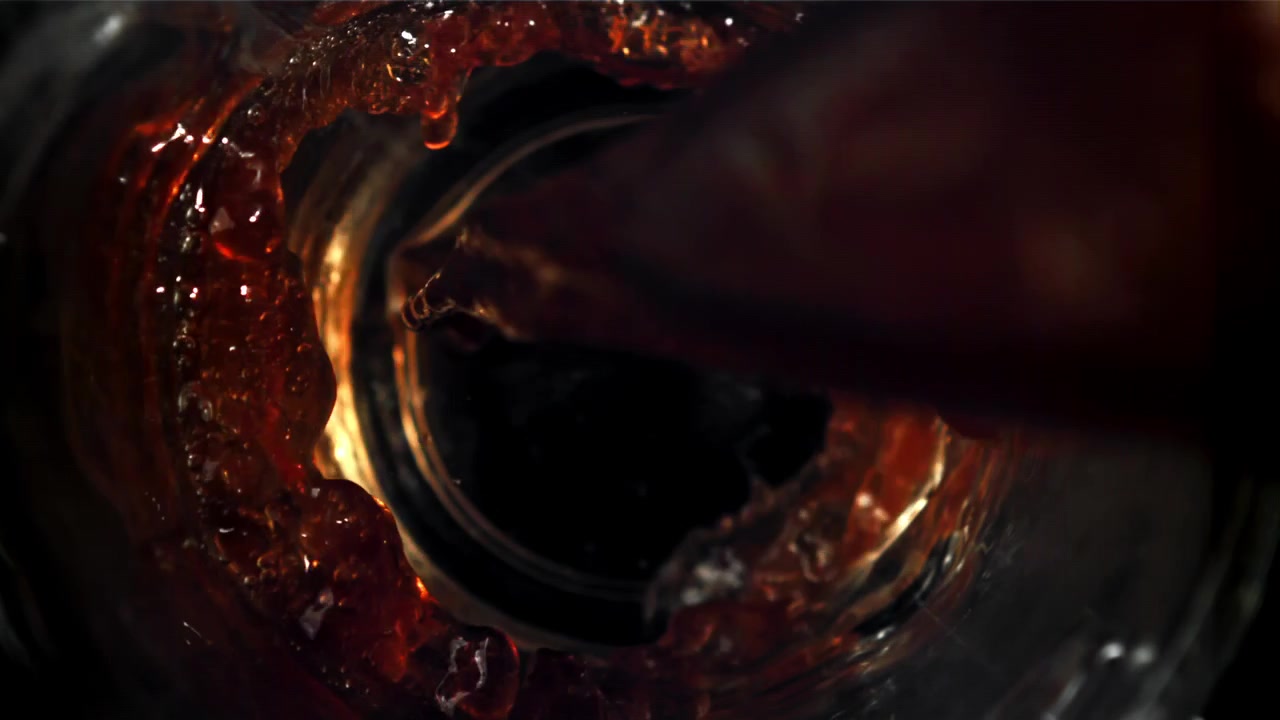 Versamento drammatico al rallentatore di liquido marrone scuro in un bicchiere