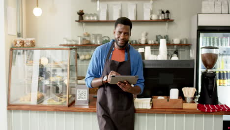 a young african american male barista stands behind a cafe counter, holding a tablet