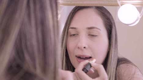 close up of young white woman putting pink lipstick on