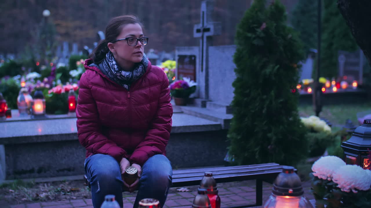 Donna triste seduta davanti a una tomba illuminata da candele accese.