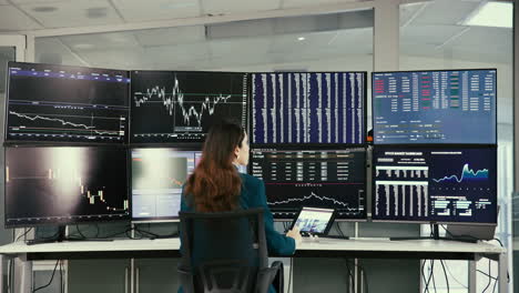 businesswoman working at a desk with multiple computer screens displaying financial data