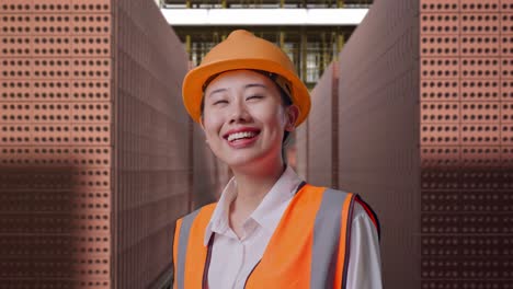 Close Up Side View Of Asian Female Engineer With Safety Helmet Looking Around While Standing With Red Brick Packed in Stacks Are Stored