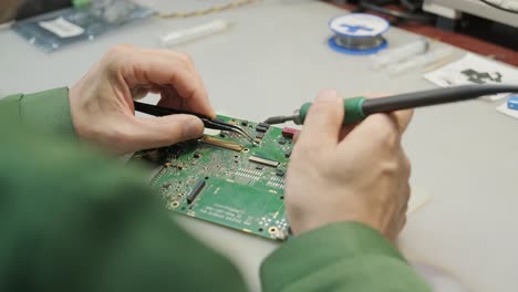 electronic equipment repair shop. the engineer technician solders the printed circuit board of an electronic device under a microscope.